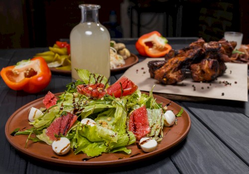 A fresh salad with leafy greens, grapefruit, mozzarella, and balsamic drizzle, alongside roasted meat and a bottle of lemonade.