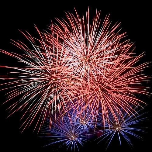Fireworks explode in the night sky, displaying vibrant red and blue bursts.