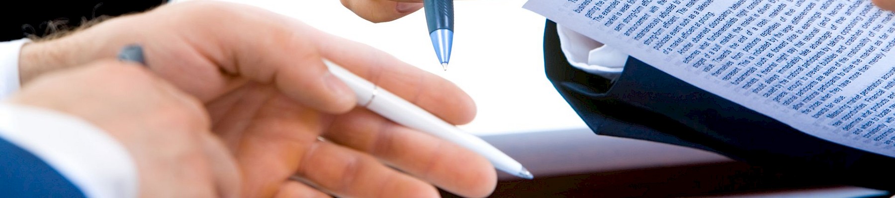 Two people exchanging pens while reviewing documents, suggesting a business or legal agreement context.