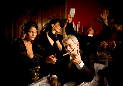 A man in a coffin with a cigar, surrounded by people, some in dramatic poses, in a dimly lit room.